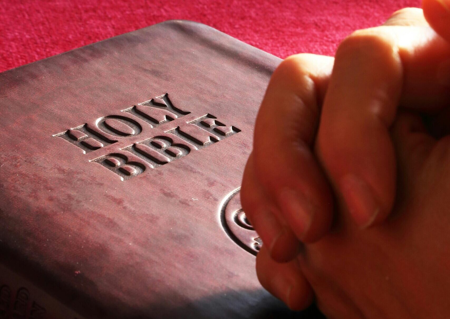 Close-up of hands praying on a Holy Bible, symbolizing faith and spirituality.
